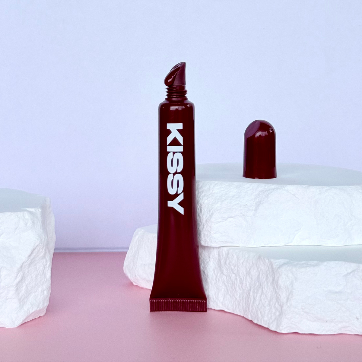 Kissy Gloss Berry worn on lips with the berry lip gloss tube held beside the face