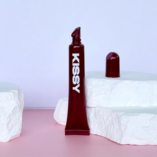 Kissy Gloss Berry worn on lips with the berry lip gloss tube held beside the face