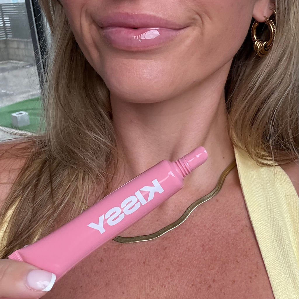 Model wearing Kissy Gloss Pink and holding the open pink lip gloss tube