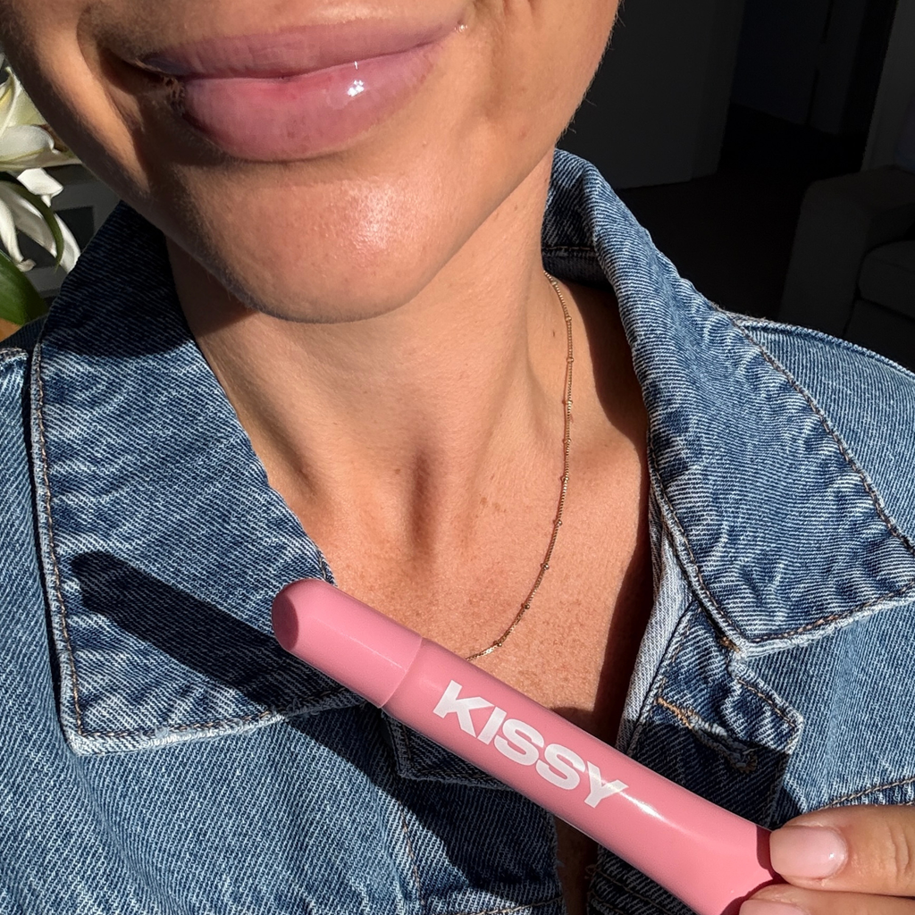 Model wearing Kissy Gloss Pink and holding the tube in natural sunlight