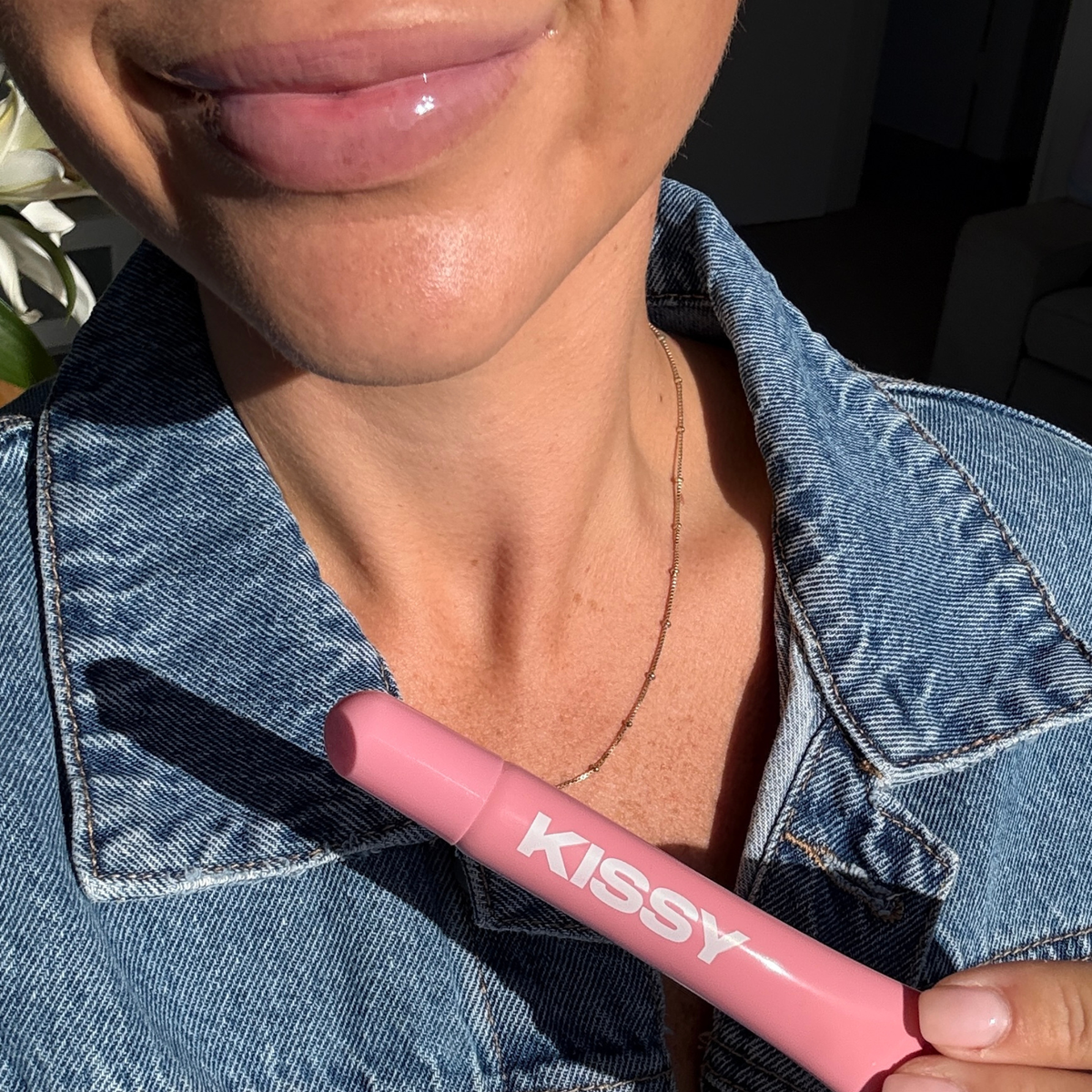 Model wearing Kissy Gloss Pink and holding the tube in natural sunlight