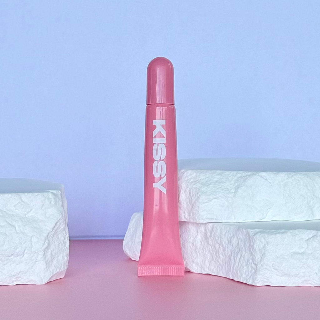 Closed tube of Kissy Gloss Pink lip gloss on a pastel product set