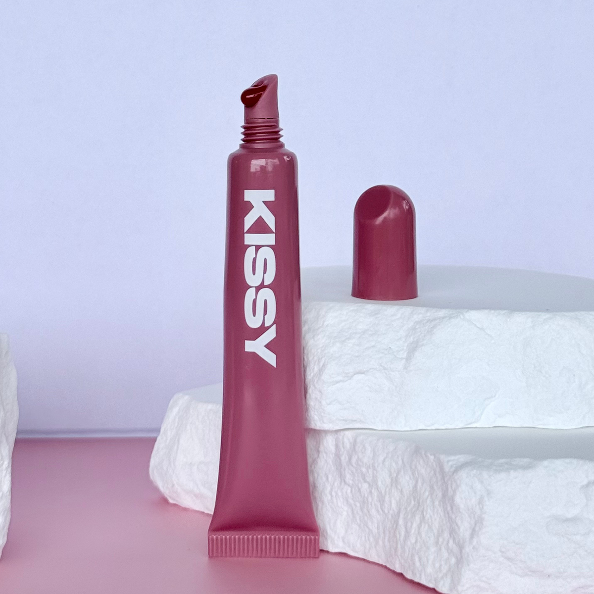 Closed Kissy Gloss Red tube standing upright against a pastel background
