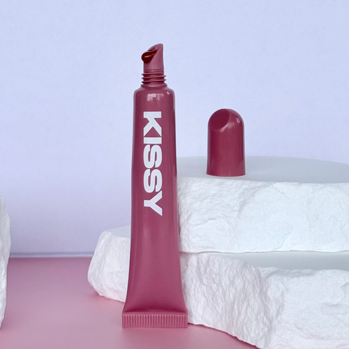 Closed Kissy Gloss Red tube standing upright against a pastel background